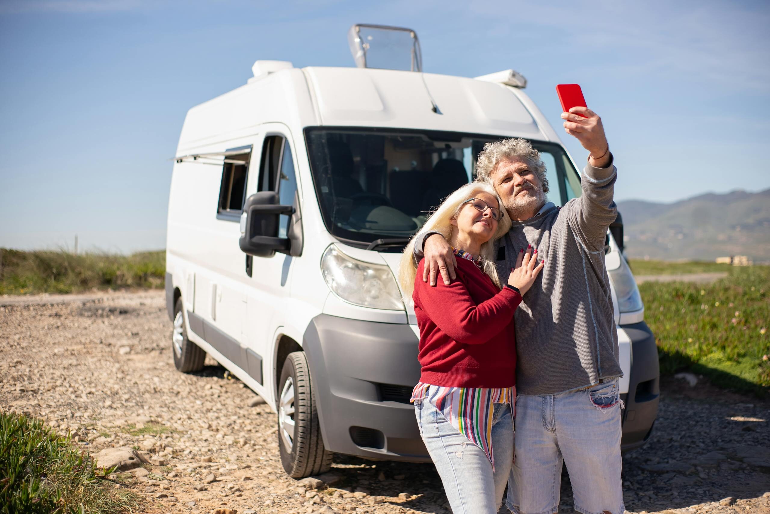 A senior couple taking a selfie with their RV in Portugal, enjoying a sunny travel adventure.