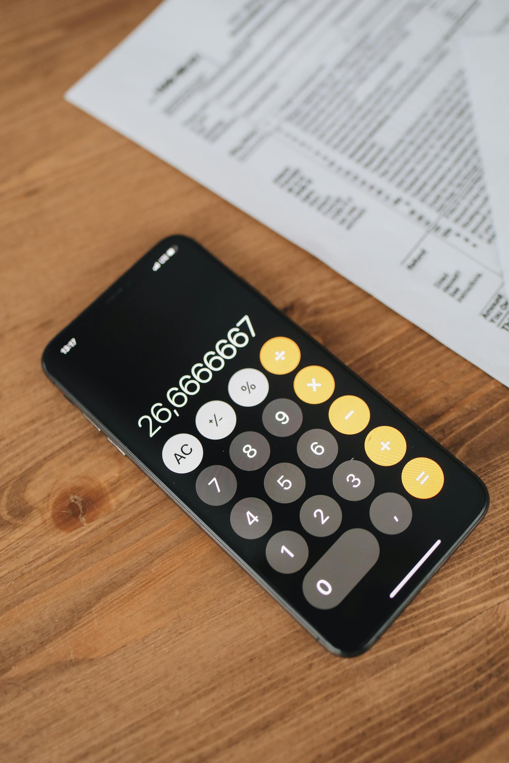 Close-up of smartphone calculator app and tax forms on a wooden desk surface.