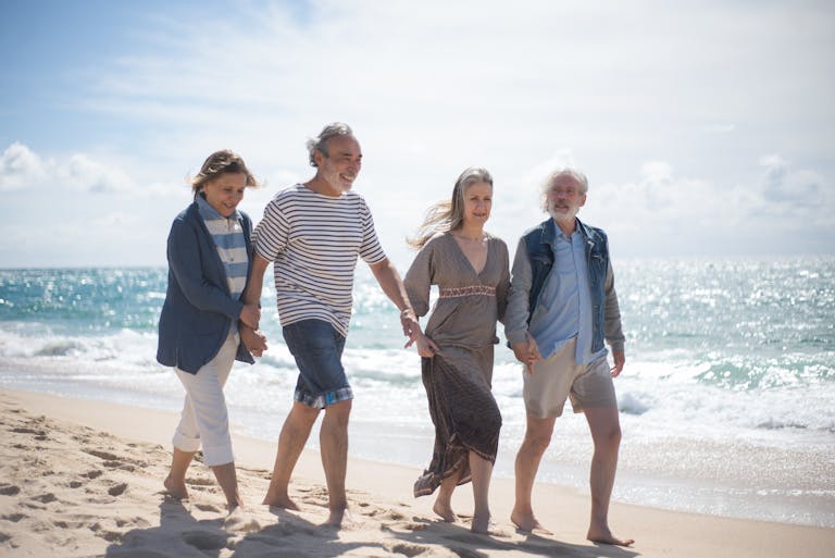 Happy senior couples walking along a sunny Portuguese beach, enjoying a leisurely day by the sea.