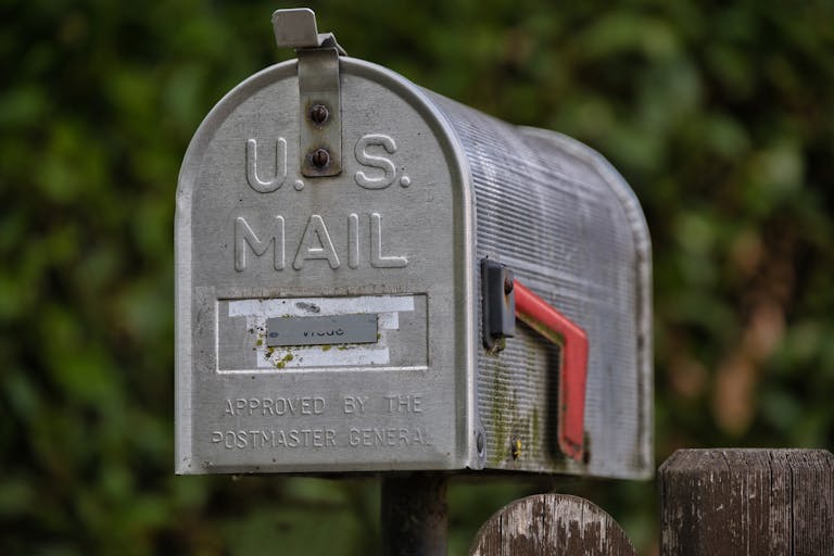 Close-up of a classic U.S. mailbox on a rustic wooden post, outdoors.