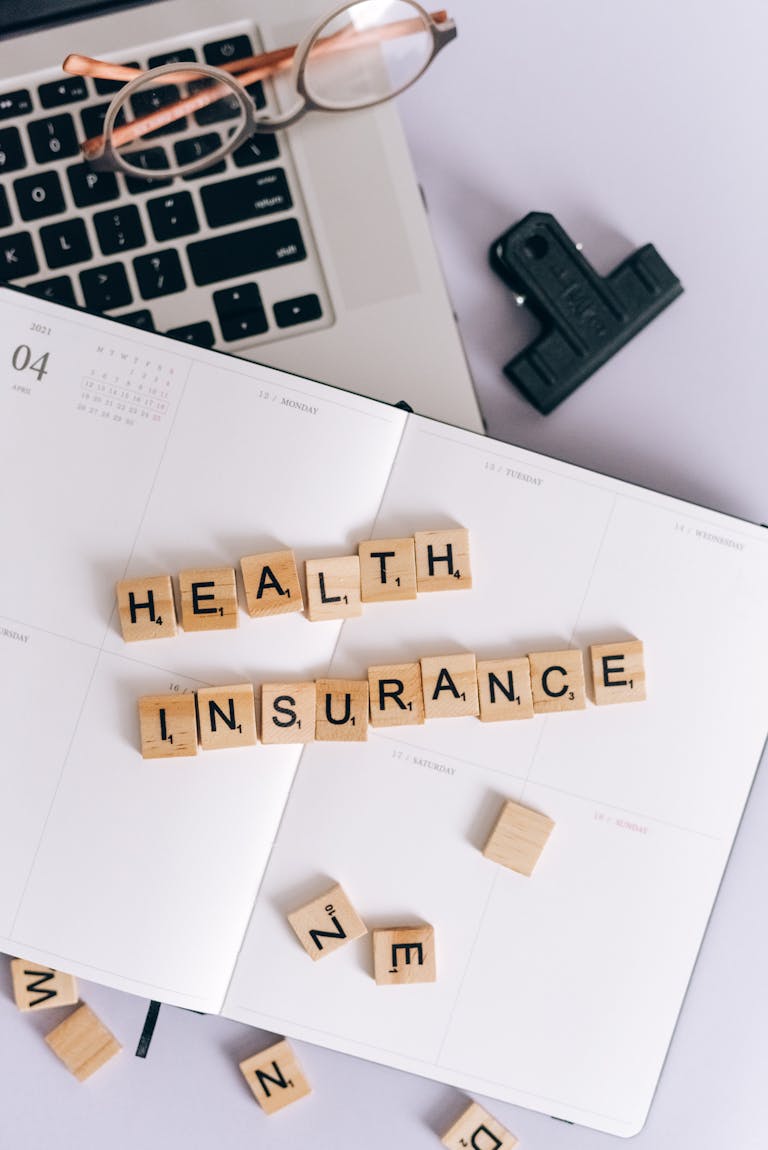 Scrabble tiles spelling 'Health Insurance' on a calendar, with laptop and stationery.