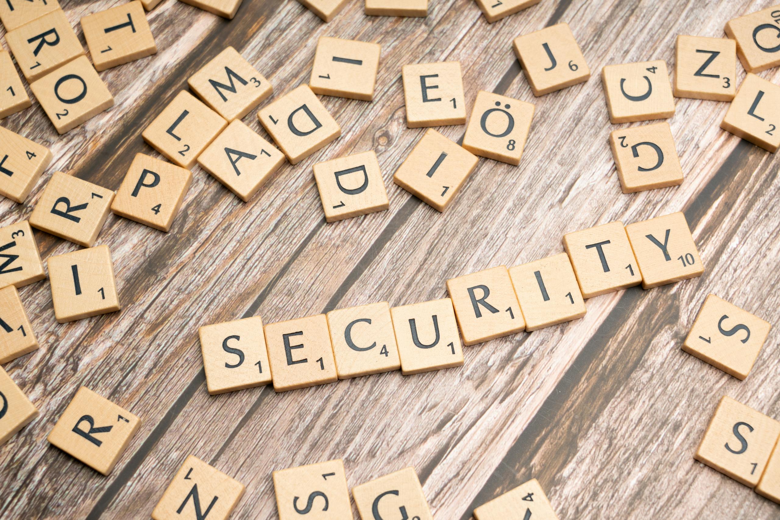 Wooden letter tiles form the word 'Security' amidst scattered tiles on wood.