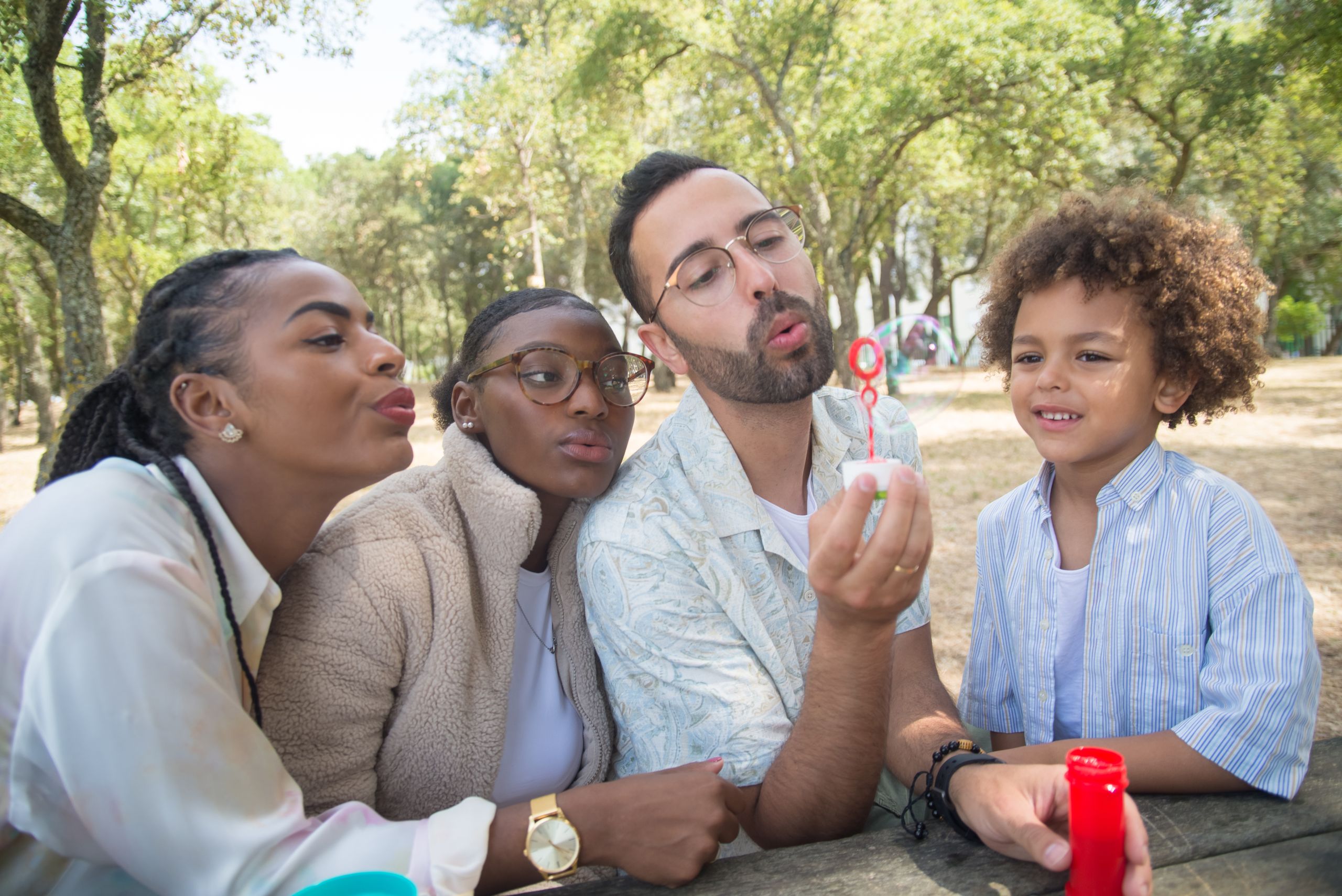 A joyful family bonding moment outdoors in a sunny park, blowing bubbles together.